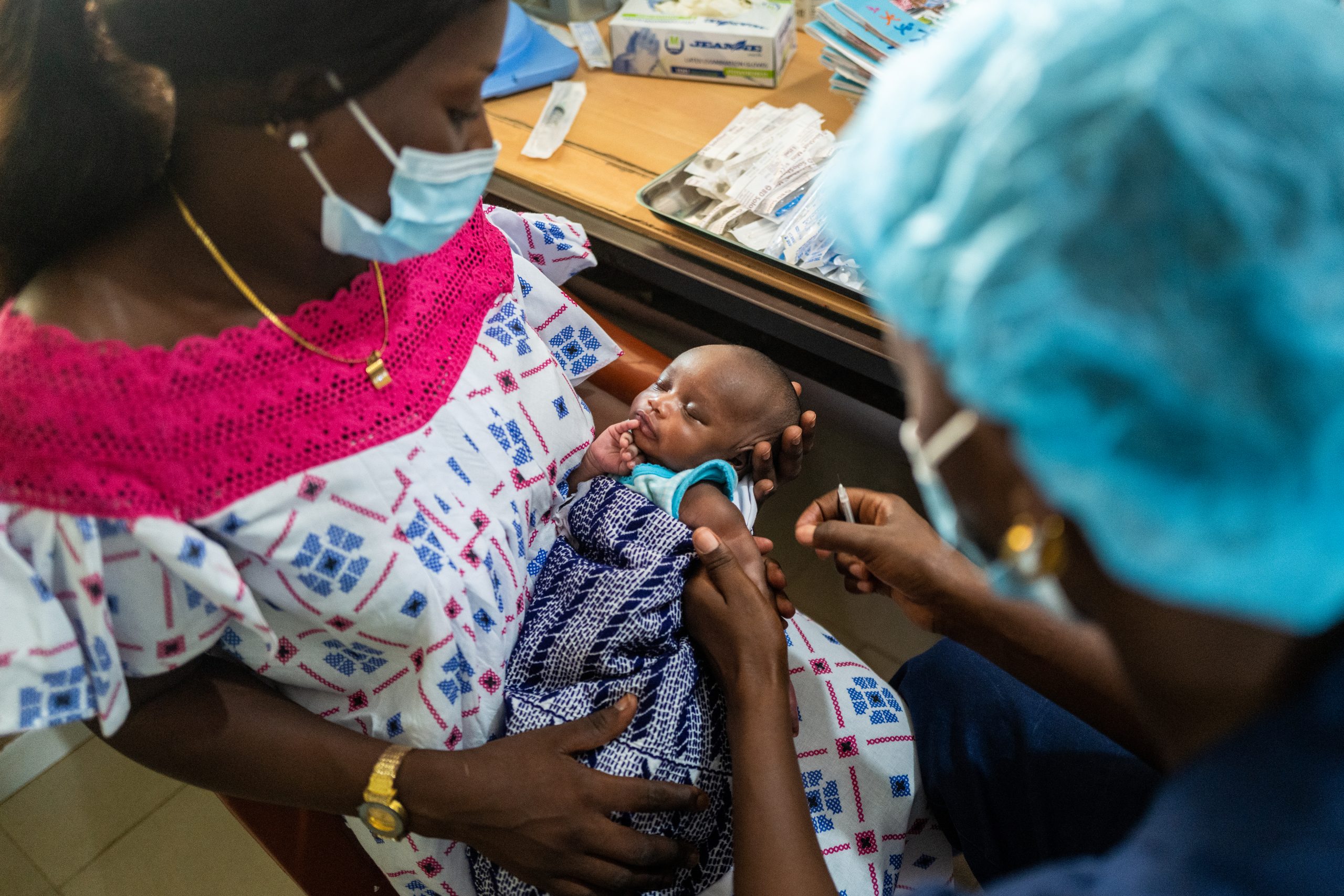 Image of a woman holding an infant about to receive a vaccination.