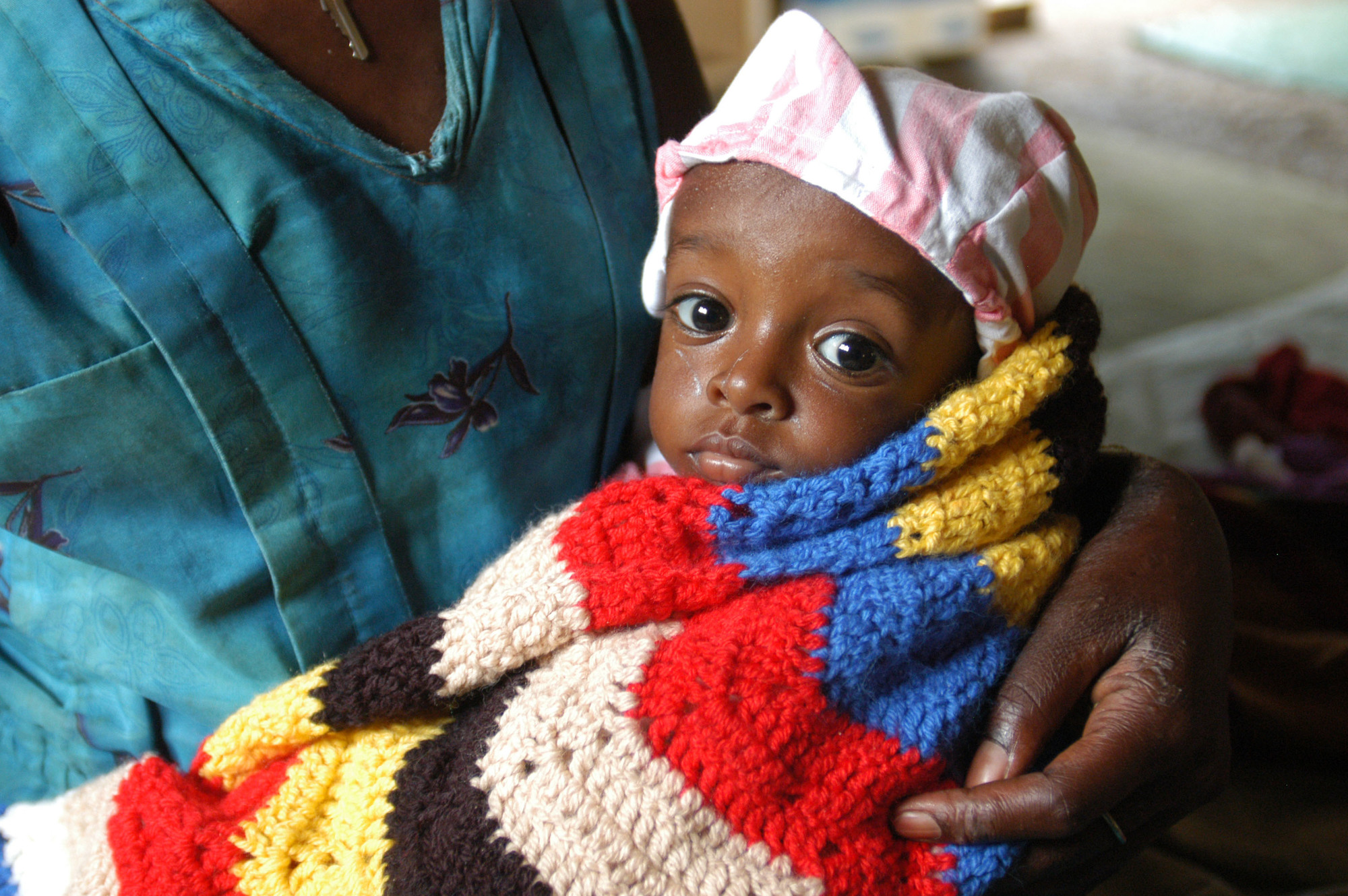 Image of an infant swaddled in a multicolor blanket.